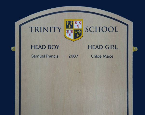Pale coloured beech veneer showing a close up of Trajan lettering and Trinity School badge